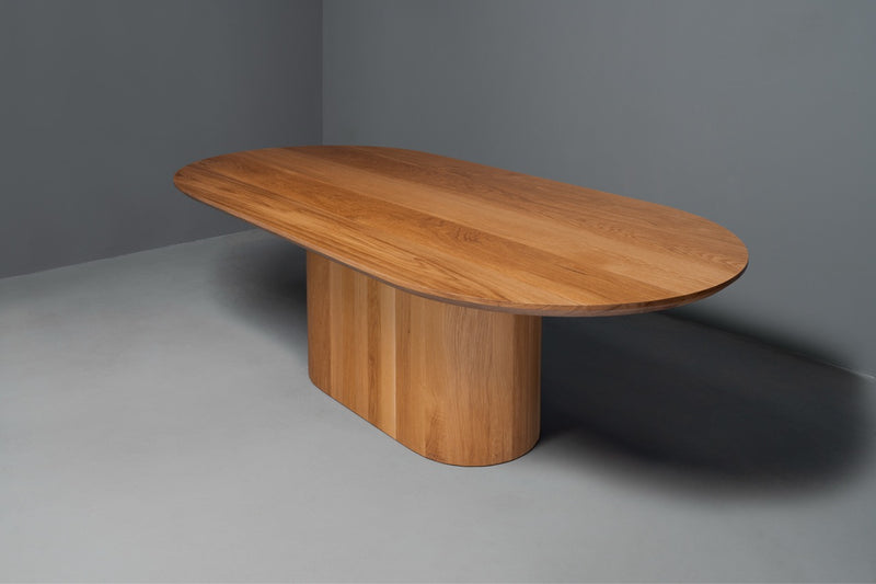 Handcrafted sustainable solid wood dining table with smooth oval top and custom modern design by expert woodworker.